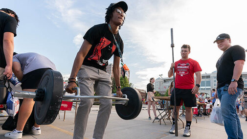 A student testing his strength by lifting weights  at the Rec Center's booth.