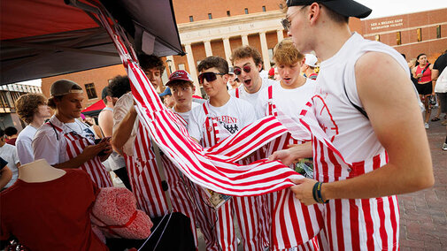 A group of students checking out red and white striped coveralls at a booth.