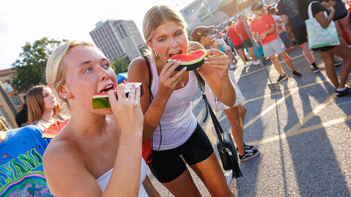 A couple of students hunched over eating watermelon.