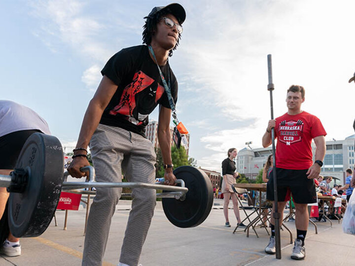 A student testing his strength by lifting weights  at the Rec Center's booth.